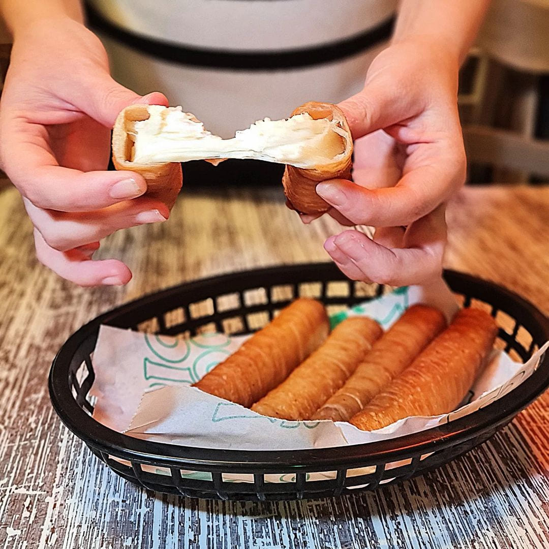 Imagen de un tequeño partido por la mitad mostrando el queso super elástico y delicioso