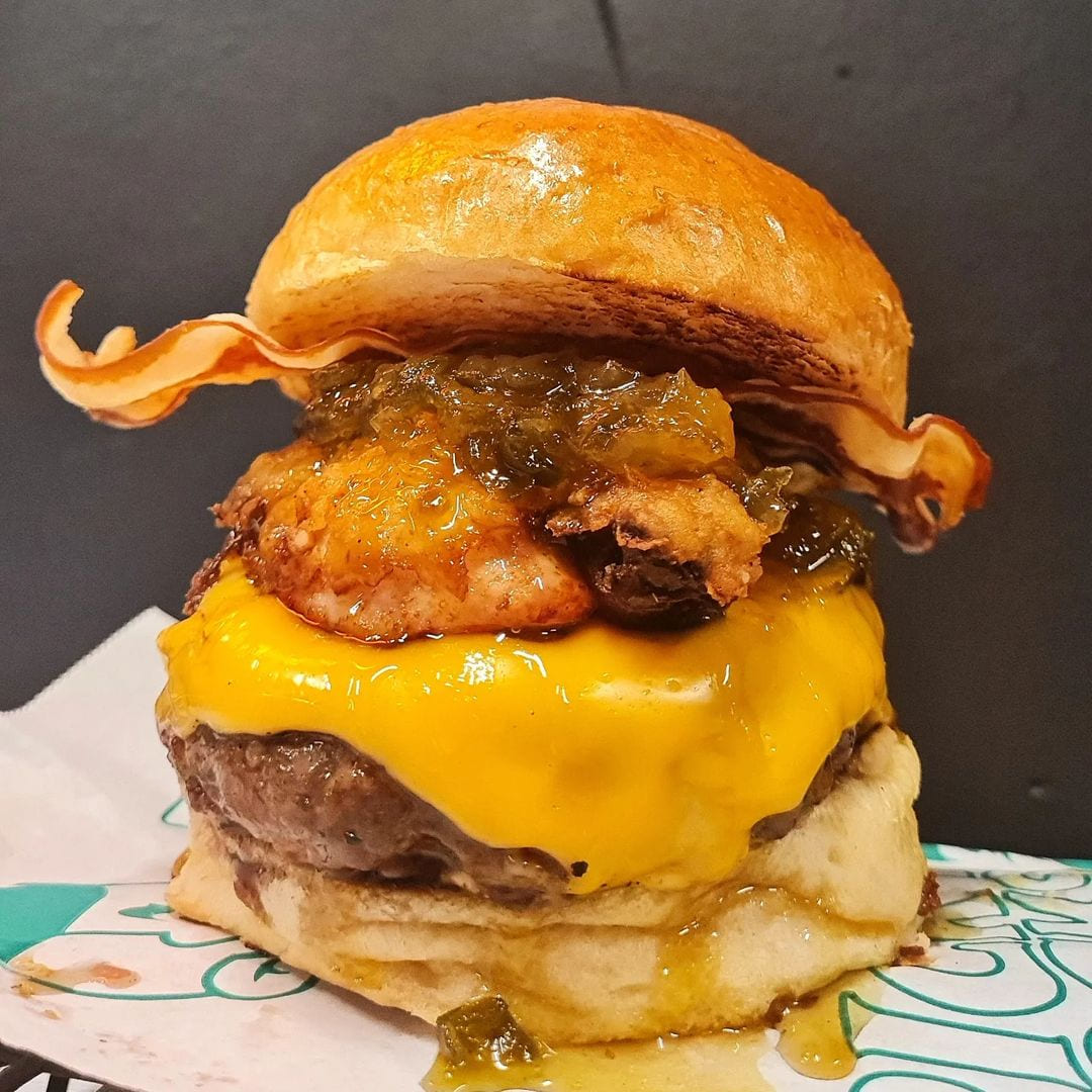 Imagen de una de las hamburguesas de medallón de Ricky Rocks, la Big Ricky con pan brioche, salsa burger, lechuga, pepinillos caseros, dry aged burger doble de 100 gramos, doble queso americano, bacon y cebolla caramelizada.